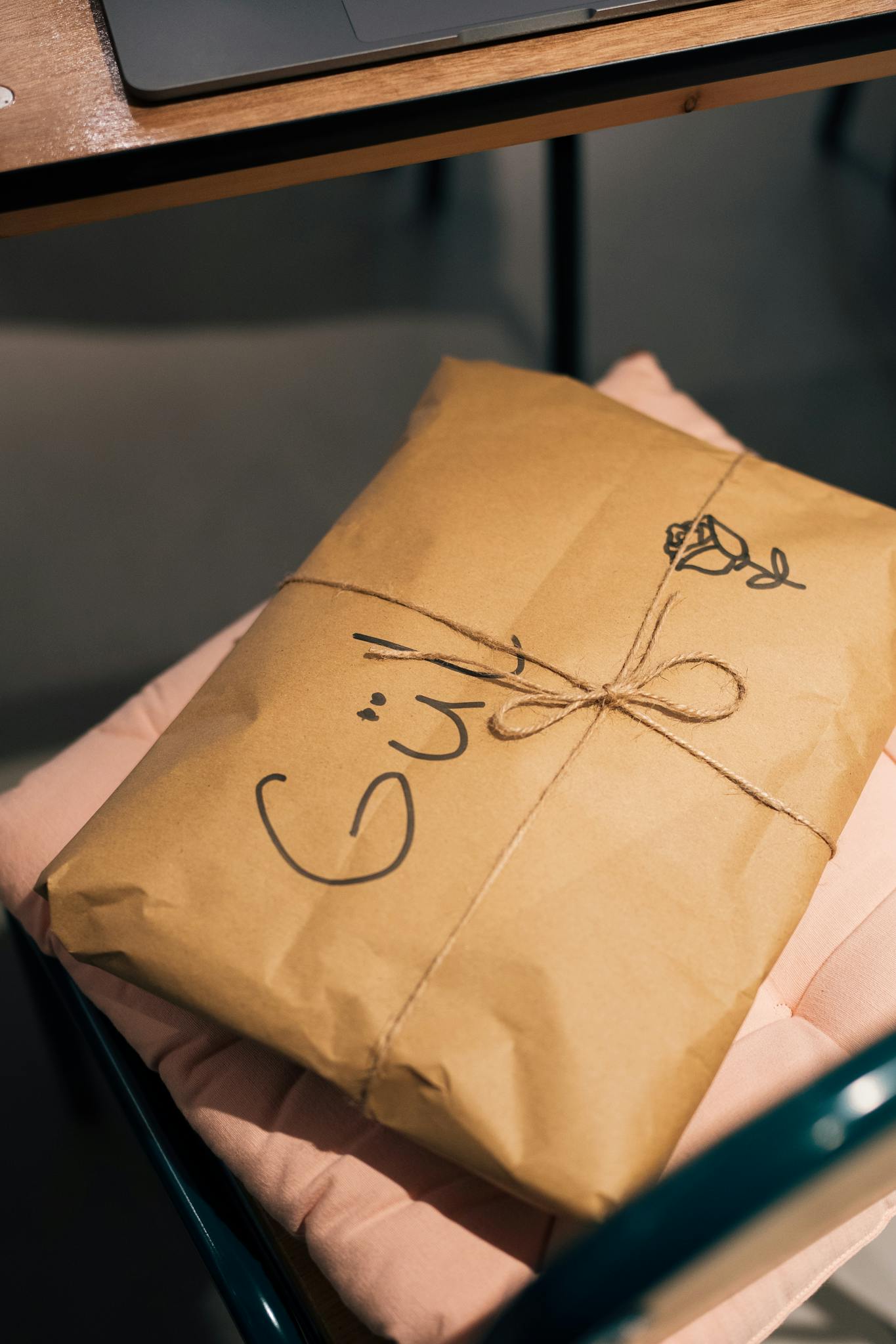 A creatively packaged gift wrapped in brown paper with handwritten text and a doodle rose.