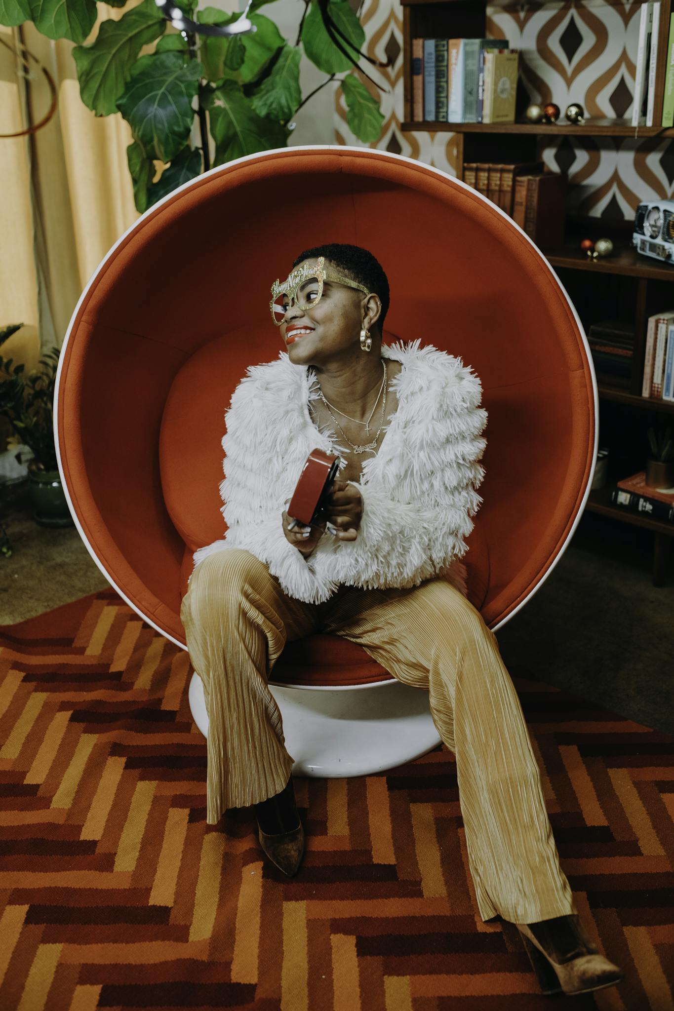 A young woman in a trendy outfit holding a gift in a vintage-style living room.