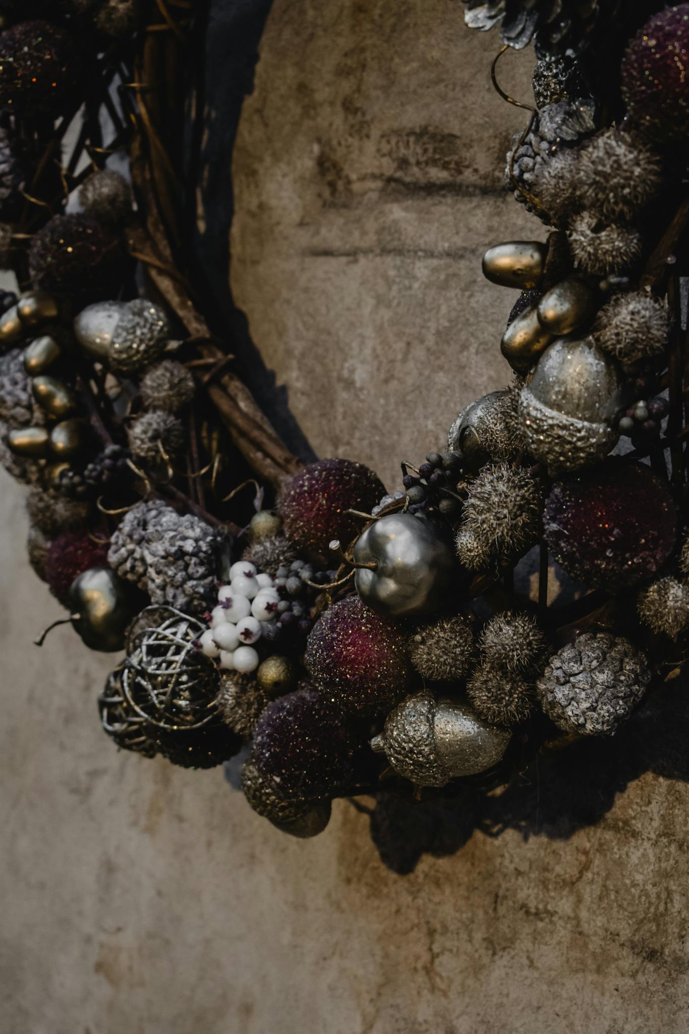 Close-up of a festive holiday wreath with metallic ornaments and berries on a textured wall.